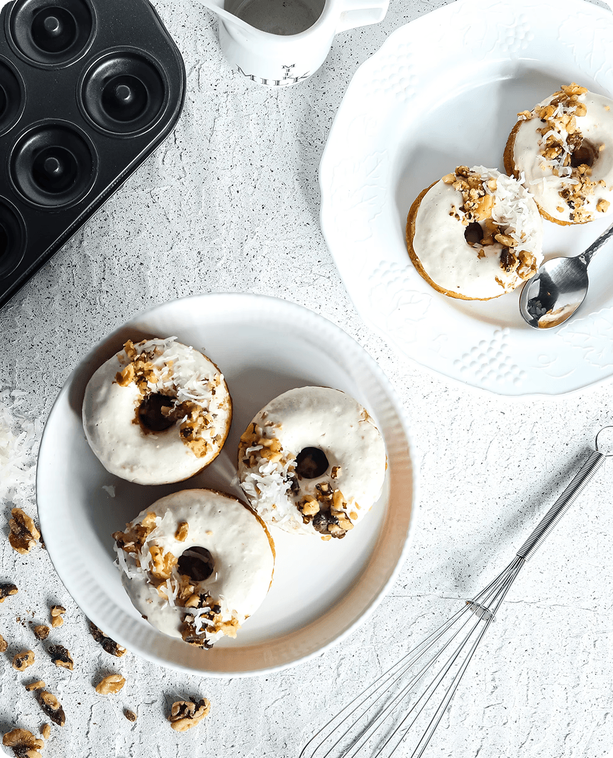 Mini donuts with white glaze, coconut flakes and nuts on white plates