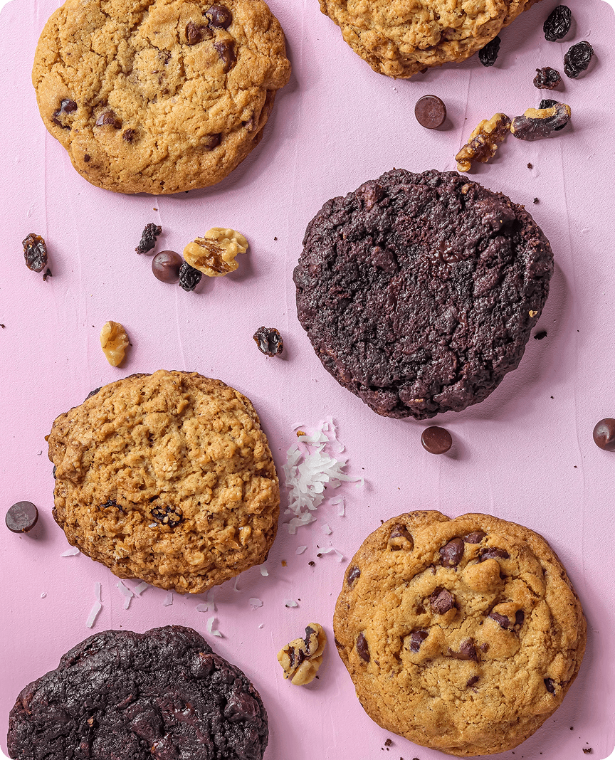 Assorted chocolate chip and chocolate cookies with nuts and raisins on a pink background